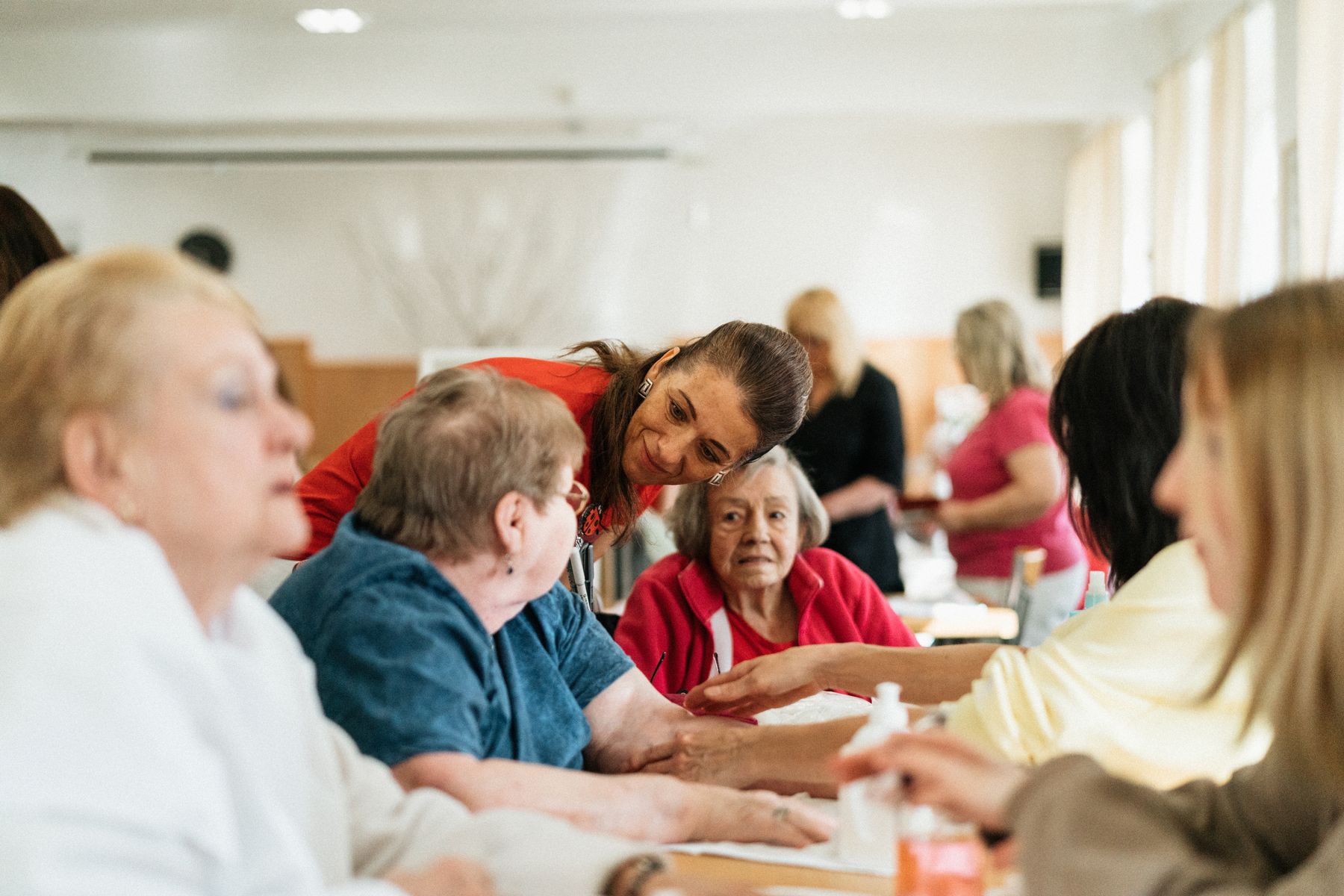 A caregiver chats with residents gathered around a dining table