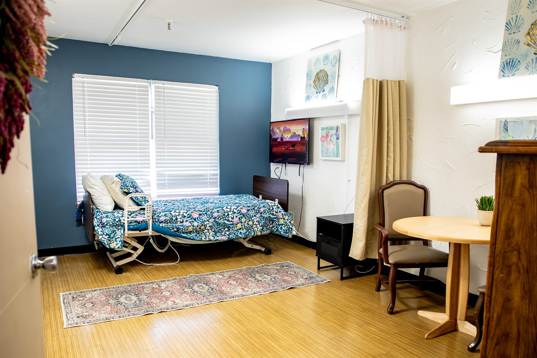 A resident room with a deep blue accent wall, floral bedding, television and a small table